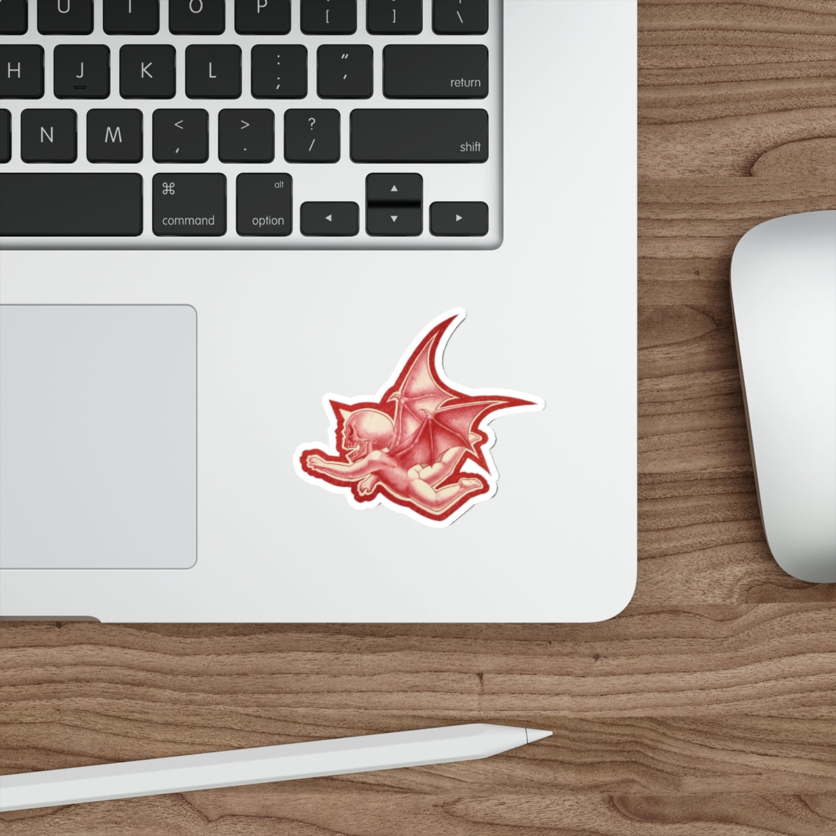 A mock up of my original design Aourim © as a sticker in Red monochrome with a white boarder of a winged creature with a skull on a white background on a mock up computer