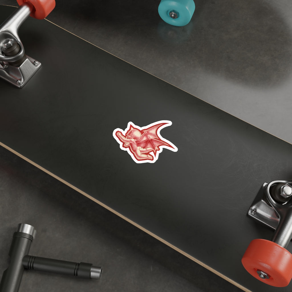 A mock up of my original design Aourim © as a sticker in Red monochrome with a white boarder of a winged creature with a skull on a white background on a mock up Skateboard